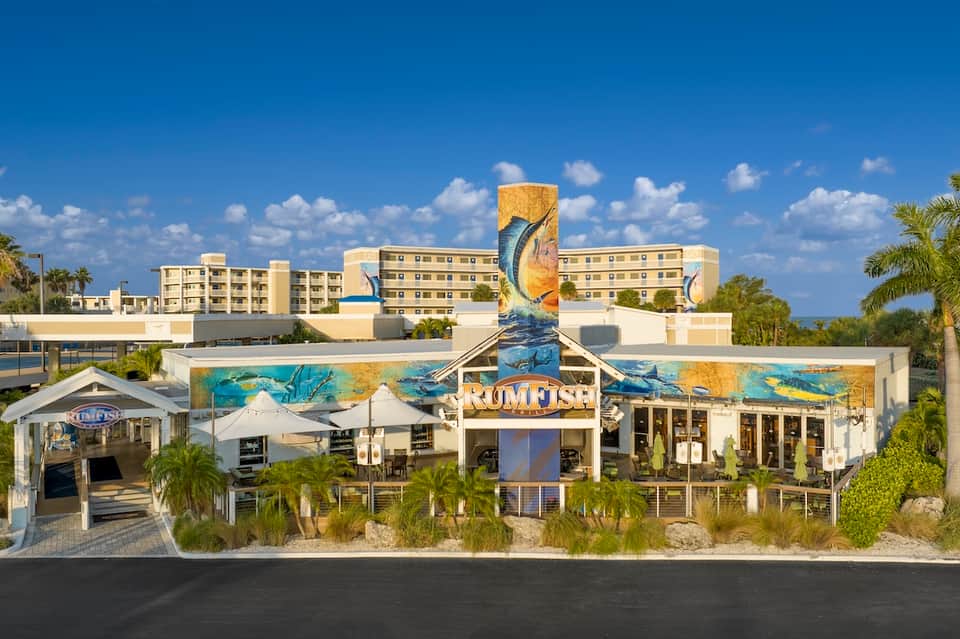 Modern beachfront resort with mural art, white tent structures, and multi-story tan buildings