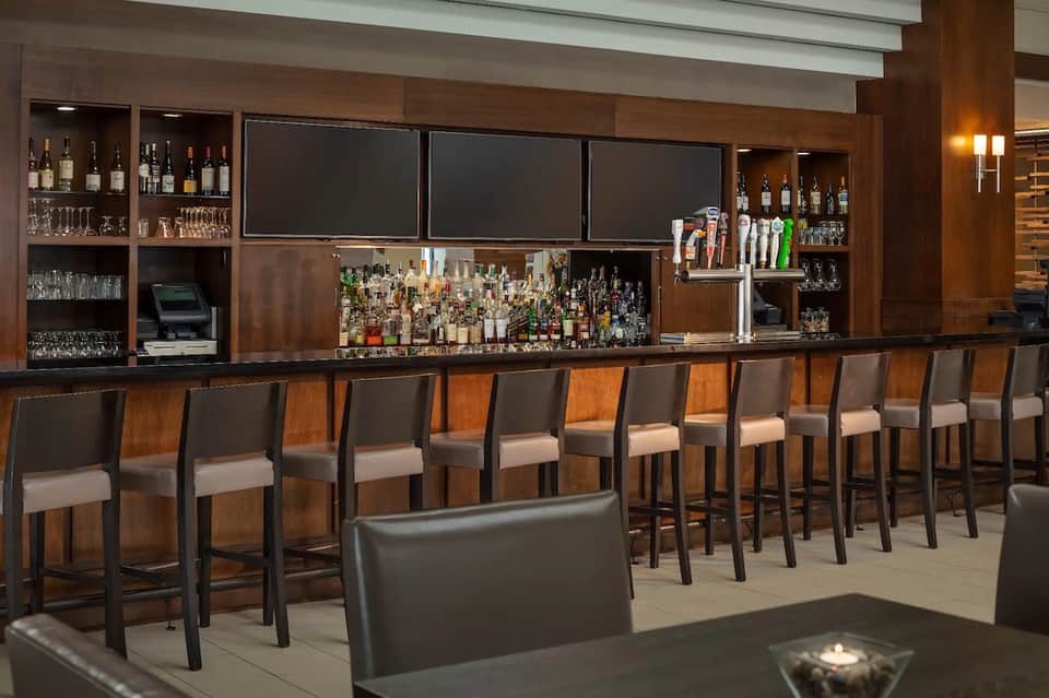 Modern bar with wooden cabinetry, extensive liquor selection, and bar stools with cushioned seating