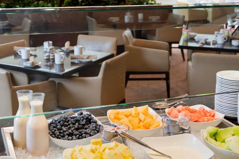 Breakfast buffet spread with fresh fruit bowls, milk pitcher, and white plates on elegant table