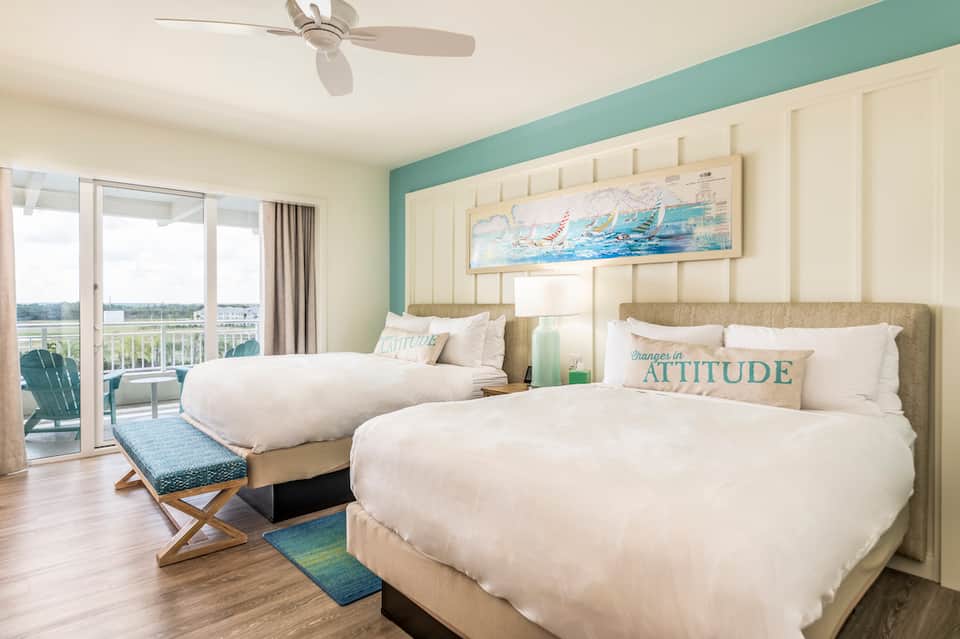 Spacious hotel room with two queen beds, balcony view, and coastal blue accent wall