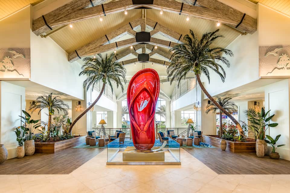 Grand hotel lobby with soaring wooden beams, palm trees, and red sculptural art installation