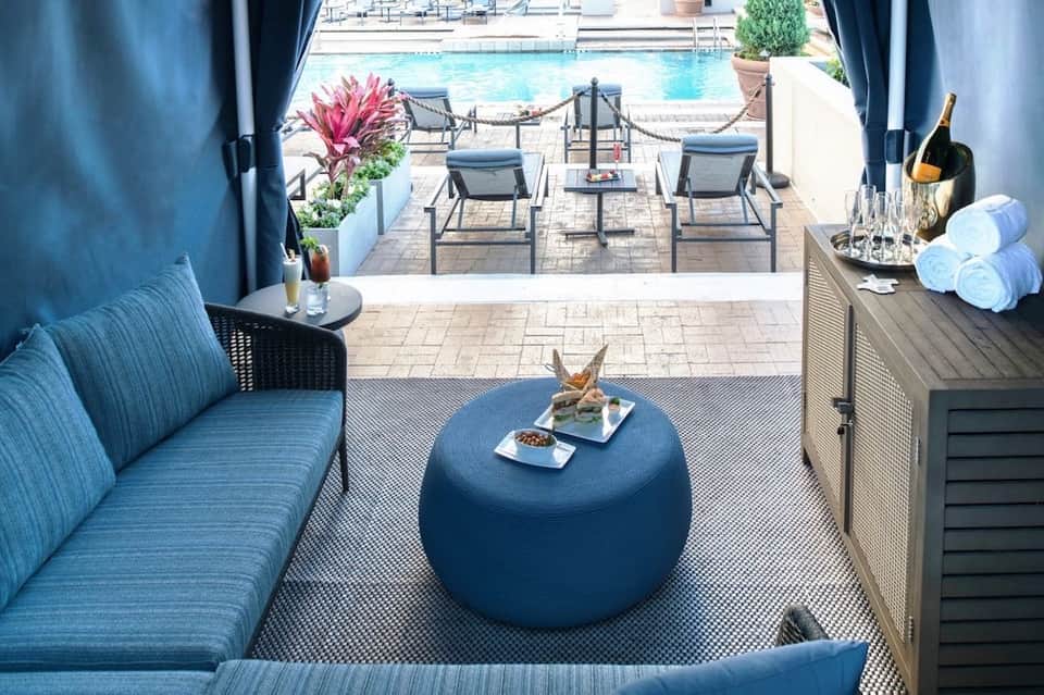 Covered poolside lounge area with blue seating, cocktails, and ocean view access