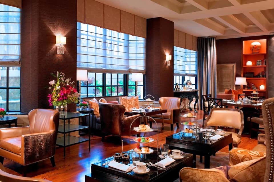 Upscale lounge with warm lighting, leather seating, floor-to-ceiling windows, and city views