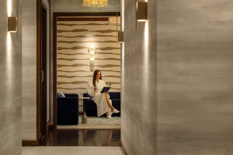 Contemporary hotel hallway with textured wall panels and woman sitting in lounge area