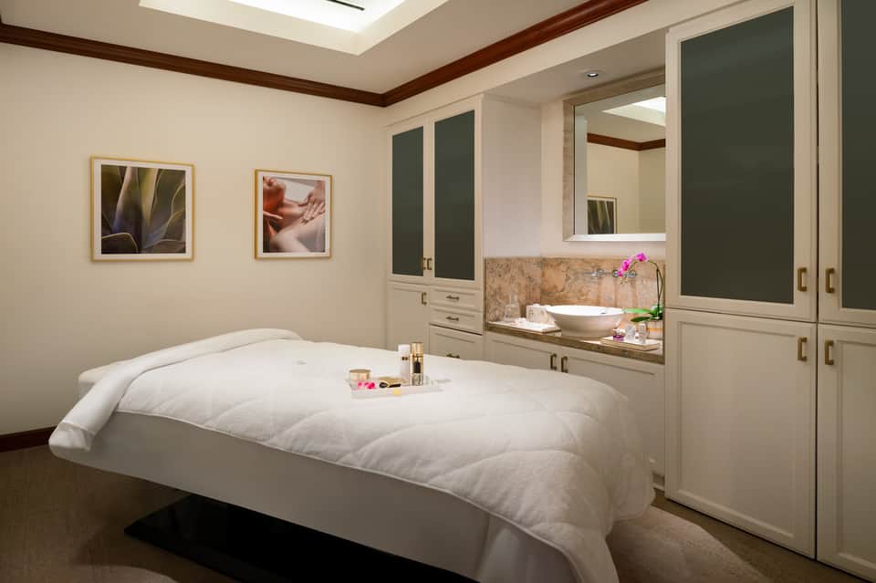 Spa treatment room with white massage bed, green cabinetry, and skylight ceiling