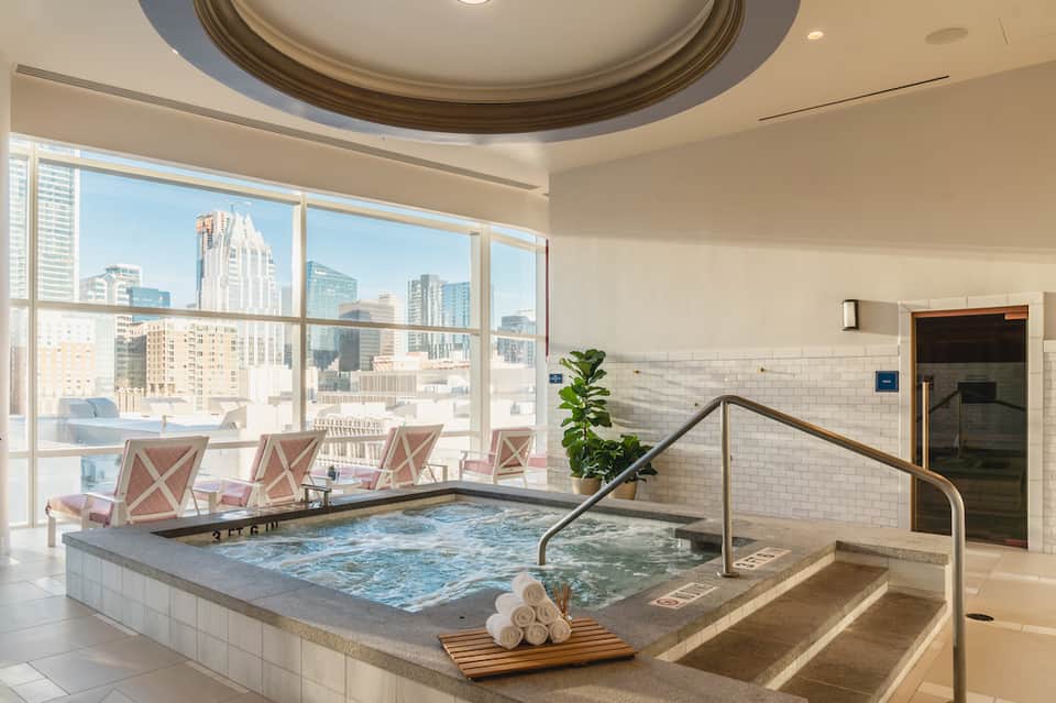 Indoor spa pool with city skyline views, white subway tiles, and lounge chairs
