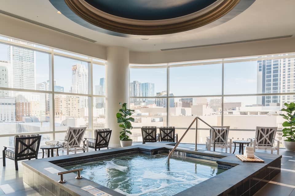 Modern indoor hot tub with city skyline views through floor-to-ceiling windows and lounge seating