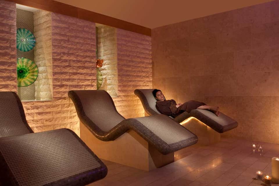 Spa relaxation room with warm lighting, stone walls, and curved lounge chairs for wellness treatments