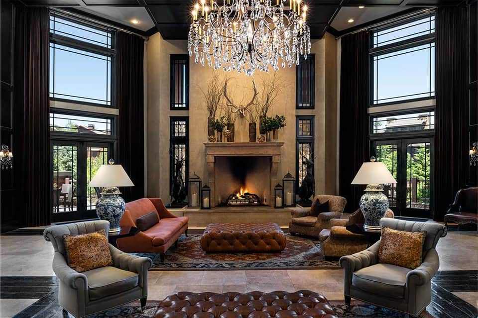 Elegant living room with fireplace, crystal chandelier, high windows, and luxurious furnishings