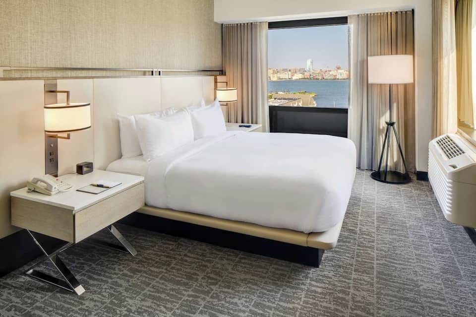 Modern hotel bedroom with queen bed, waterfront city views, floor-to-ceiling windows, and contemporary furnishings