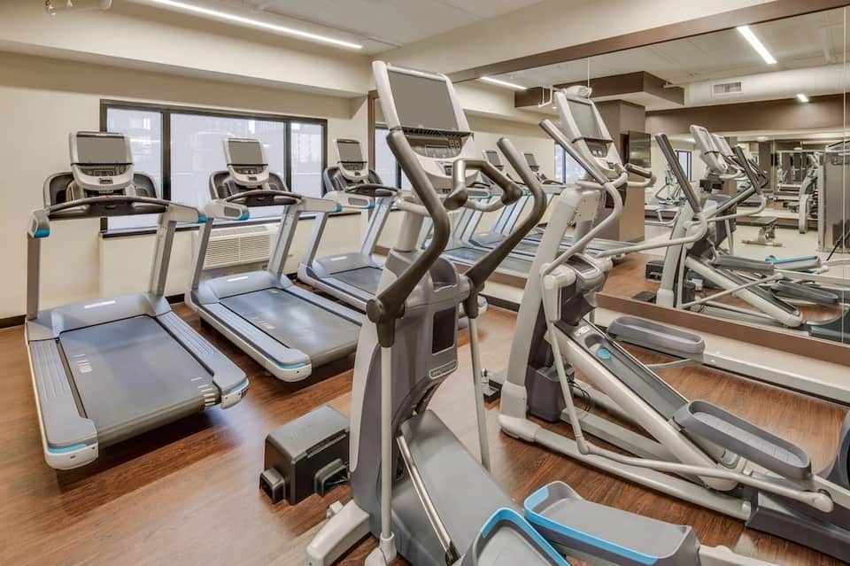 Cardio exercise room with treadmills and elliptical machines facing mirrors and large windows