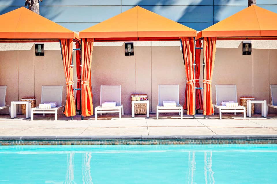 Poolside cabanas with orange umbrellas and white loungers beside turquoise swimming pool
