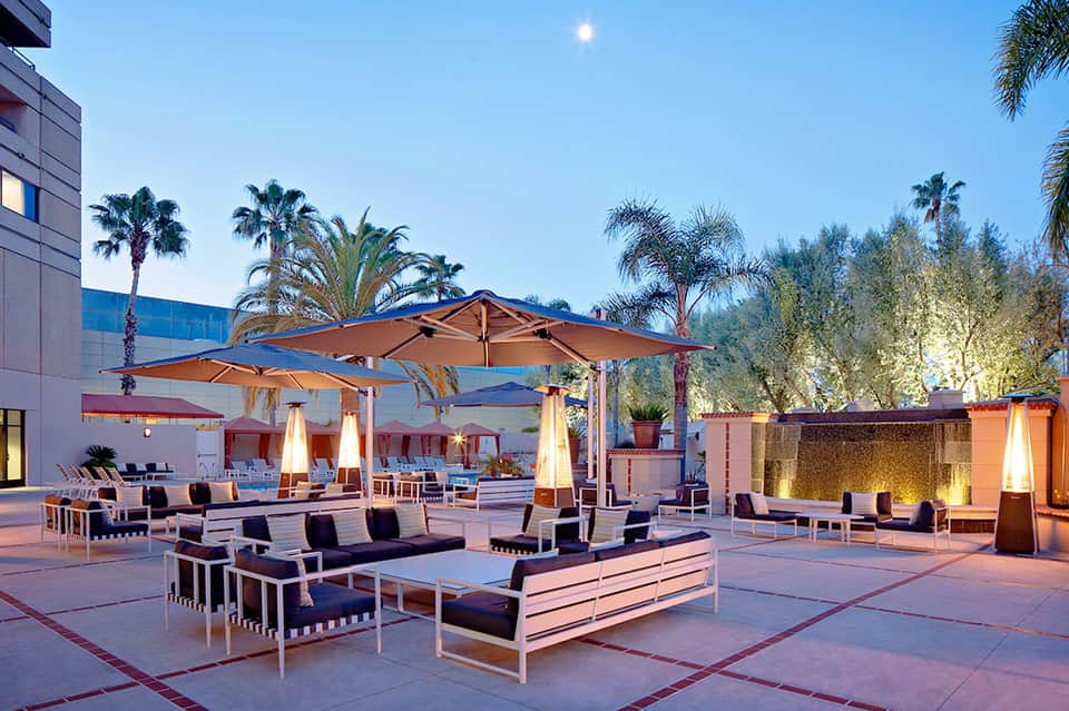 Modern resort courtyard at dusk with lounge seating, umbrellas, and palm trees