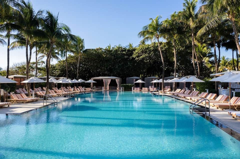 Luxurious resort pool with turquoise water, palm trees, white umbrellas, and lounge chairs