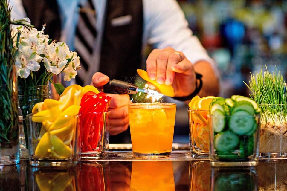 Colorful cocktails being prepared at a bar with fresh citrus garnishes and flowers