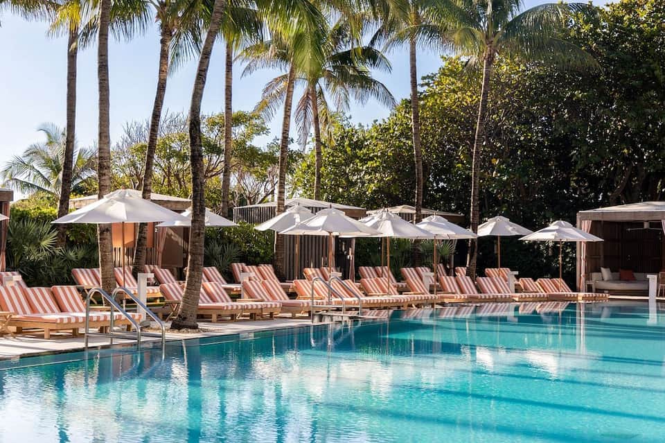 Resort pool with striped lounge chairs, palm trees, and white umbrellas