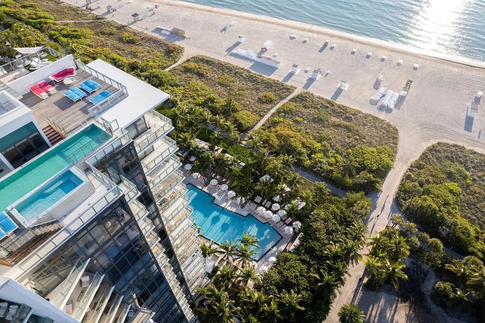 Aerial view of beachfront resort with multiple pools, sun loungers, lush tropical vegetation, and ocean access