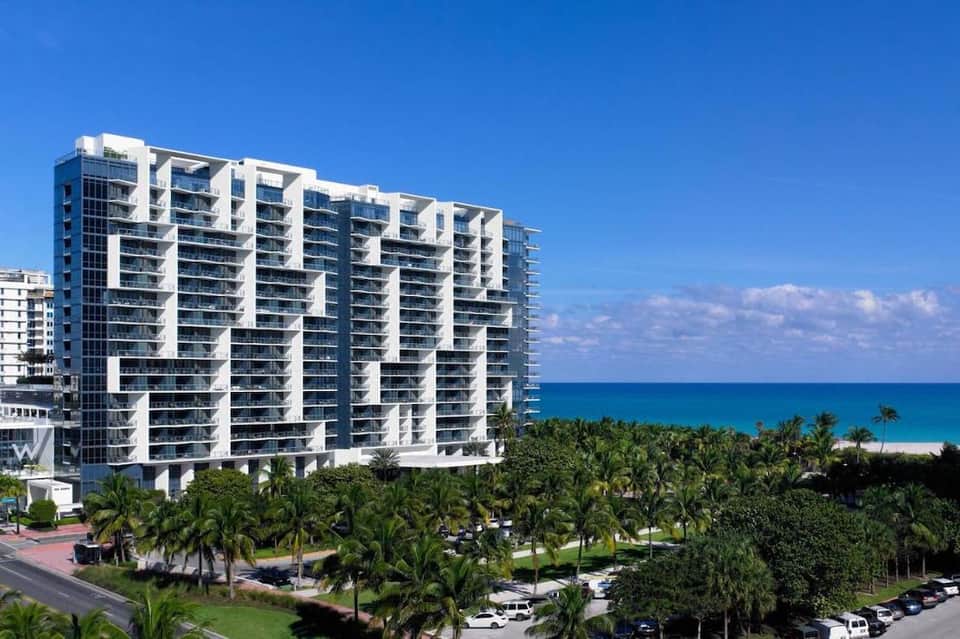 Beachfront high-rise residential building with balconies overlooking palm trees and turquoise ocean