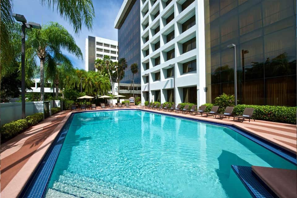 Resort outdoor swimming pool surrounded by palm trees and modern white hotel buildings