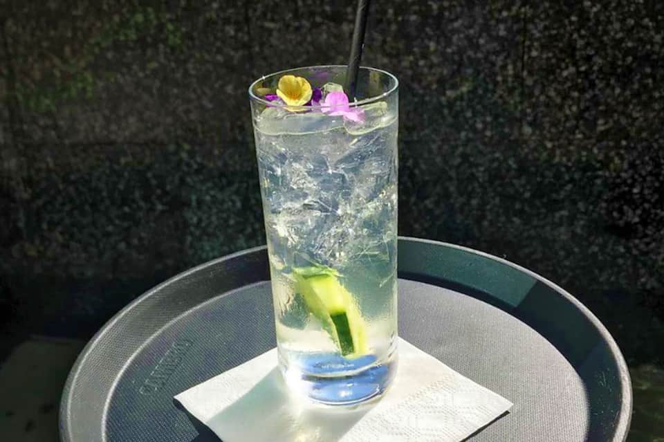 Elegant cocktail with lime slice and edible flowers on a round table with hedged background