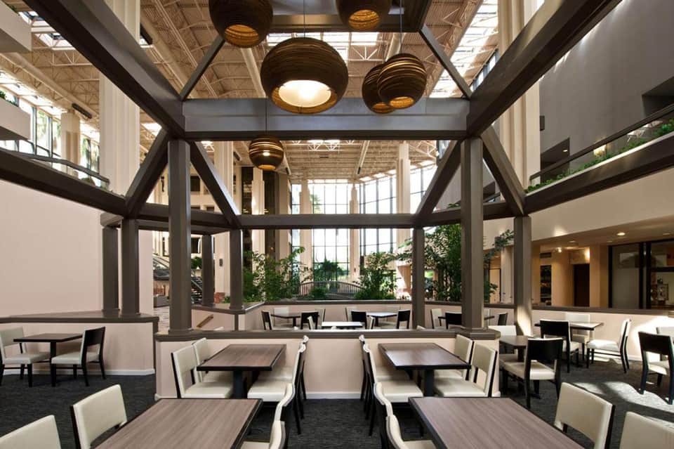 Modern dining area with wooden tables, chairs, industrial ceiling beams, and natural skylighting