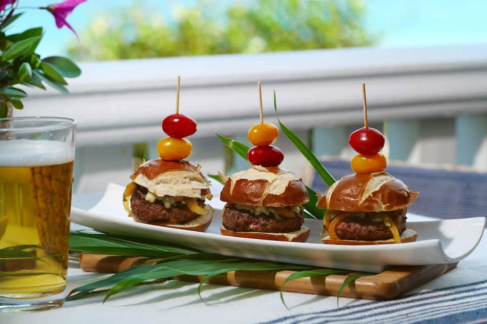 Three gourmet sliders with cherry tomato garnish and beer by pool