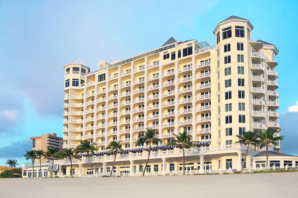 Yellow beachfront resort building with multiple stories and palm trees on sandy beach