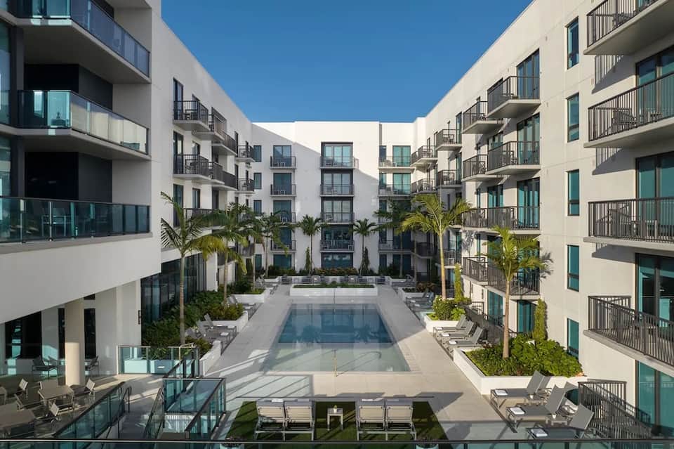 Courtyard pool surrounded by white residential buildings with balconies and palm trees