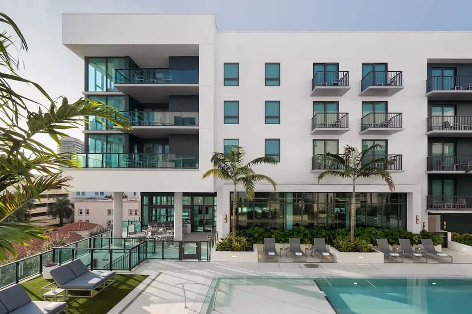 Contemporary residential building with curved balconies, pool area, loungers, and palm trees in daylight