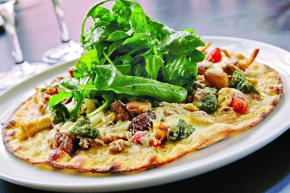 Gourmet omelet topped with fresh arugula and vegetables on white plate