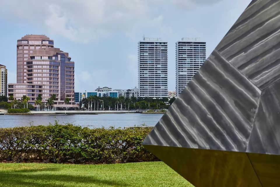Waterfront view of high-rise residential towers and palm trees along a river with architectural detail in foreground