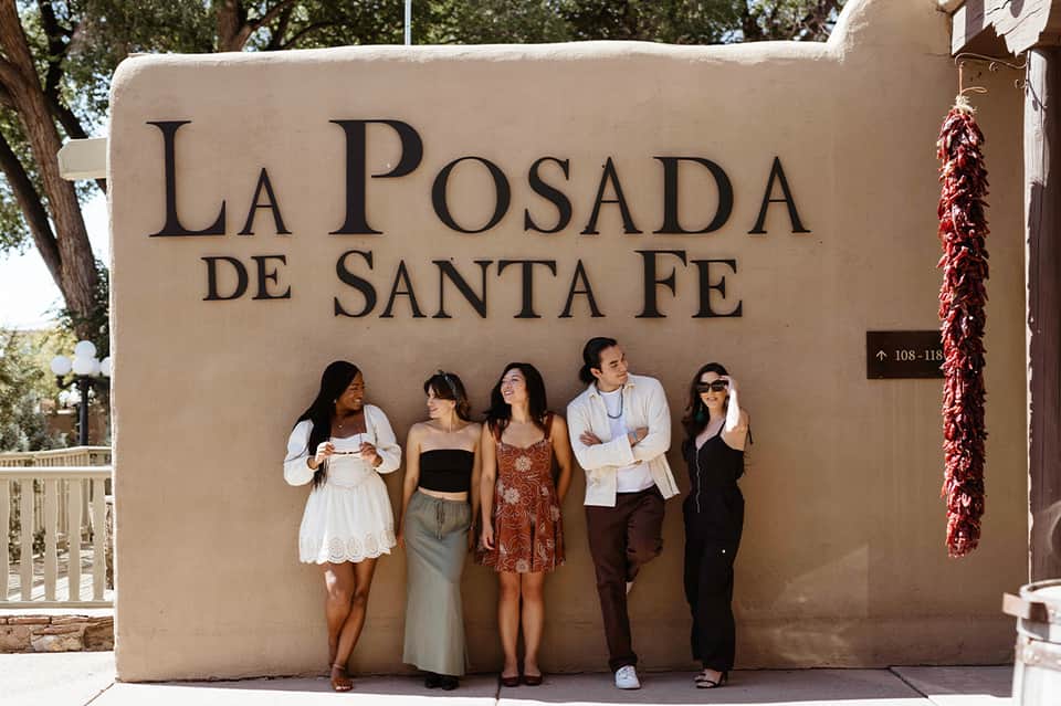 Five guests posing in front of La Posada de Santa Fe sign on stucco wall