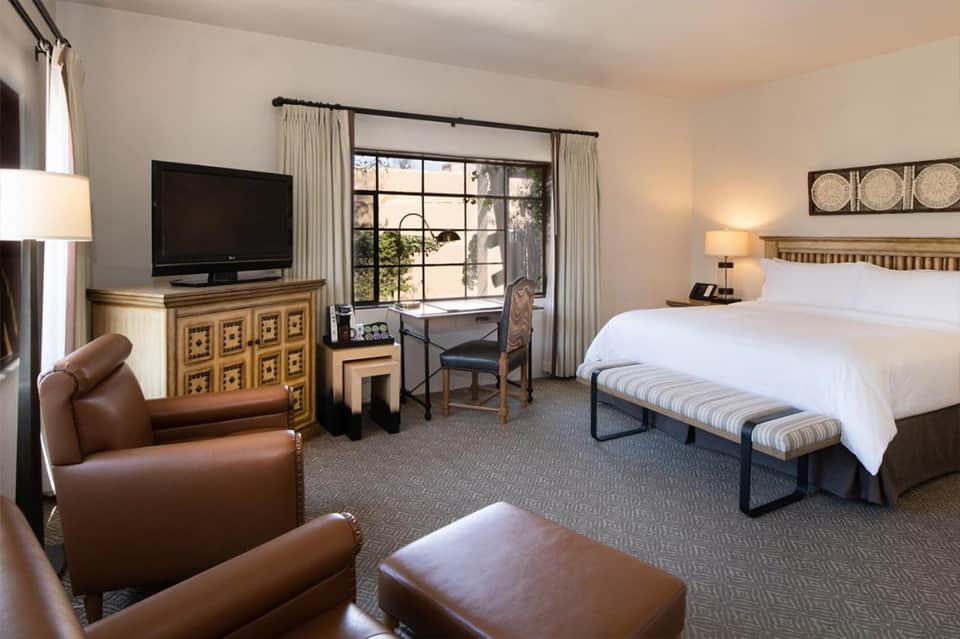 Spacious hotel suite with king bed, leather seating, TV, and sliding glass doors to balcony