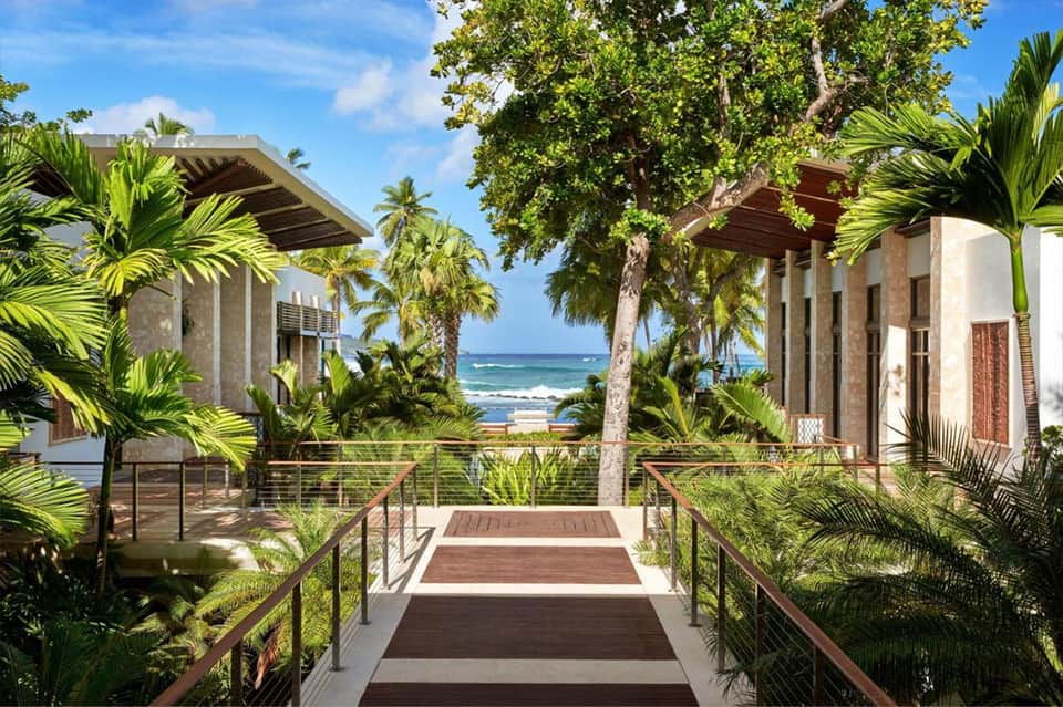 Beachfront resort walkway lined with palm trees leading to ocean view with modern architectural structures