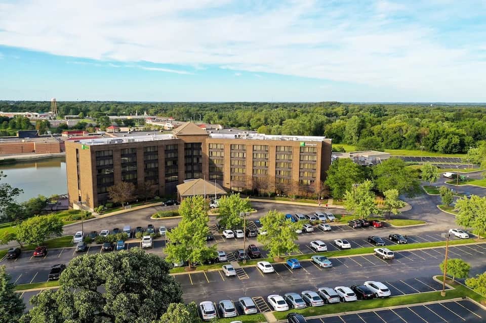 Aerial view of modern riverside hotel building with parking lot and surrounding green landscape