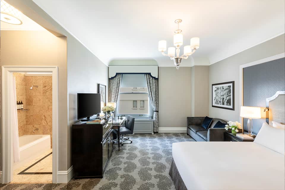 Spacious hotel room with queen bed, desk, sitting area, and modern furnishings