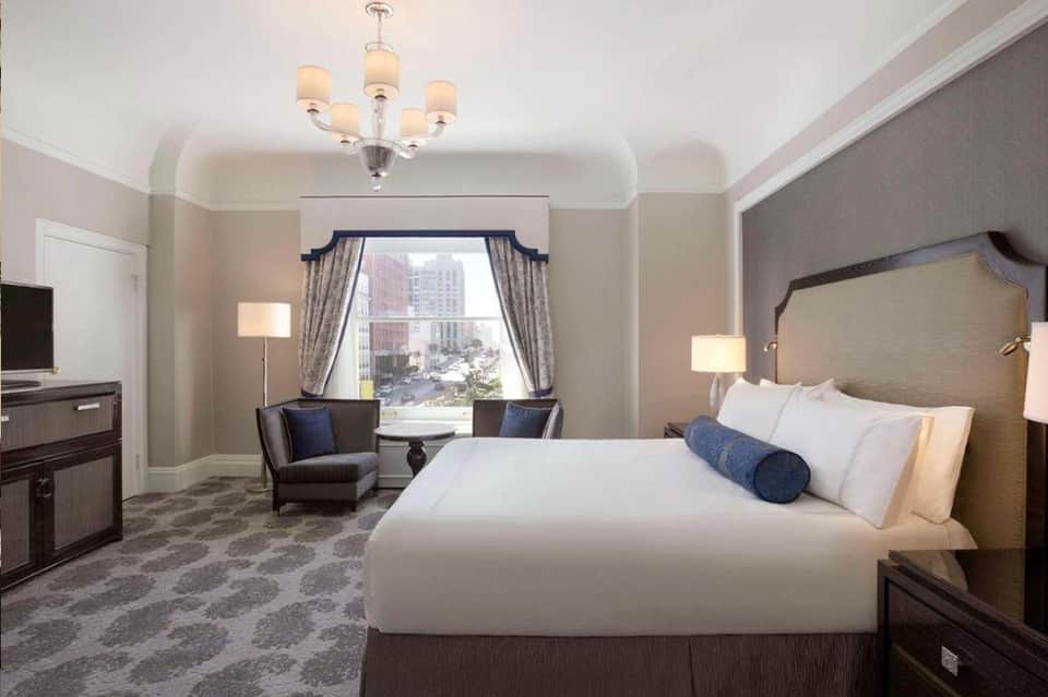 Luxury hotel suite with king bed, window seating area, chandelier, and city skyline views