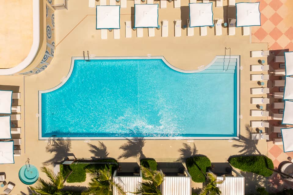 Aerial view of rectangular resort pool surrounded by lounge chairs and palm tree landscaping on sandy deck
