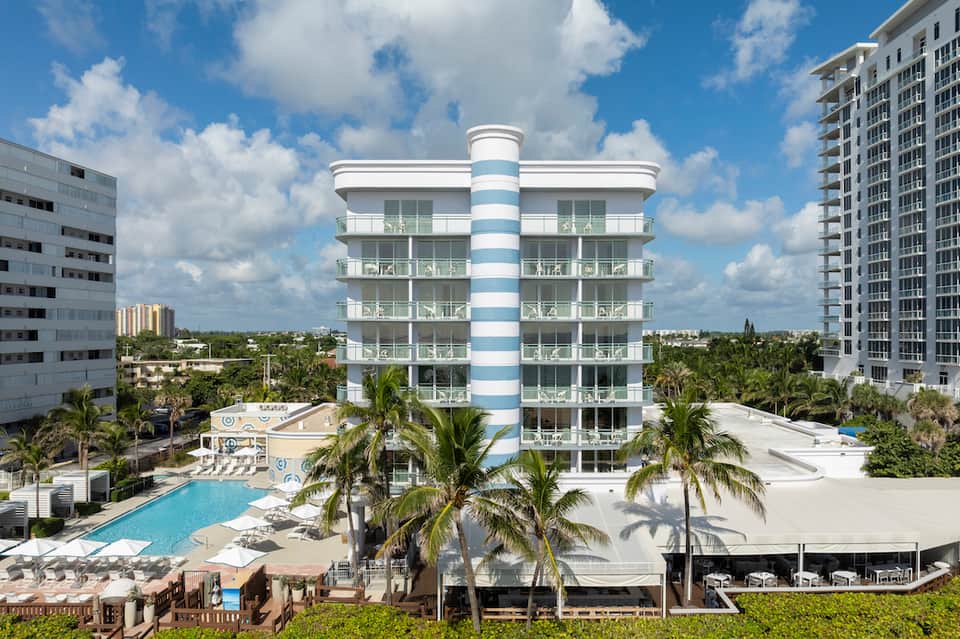 Beachfront resort with distinctive white and blue striped tower building, palm trees, and ocean view