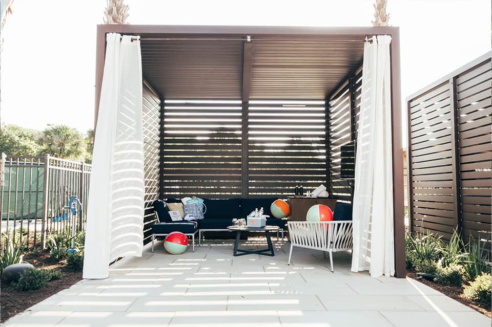Modern outdoor pavilion with lounge seating, fire pit, and white curtains under a metal pergola