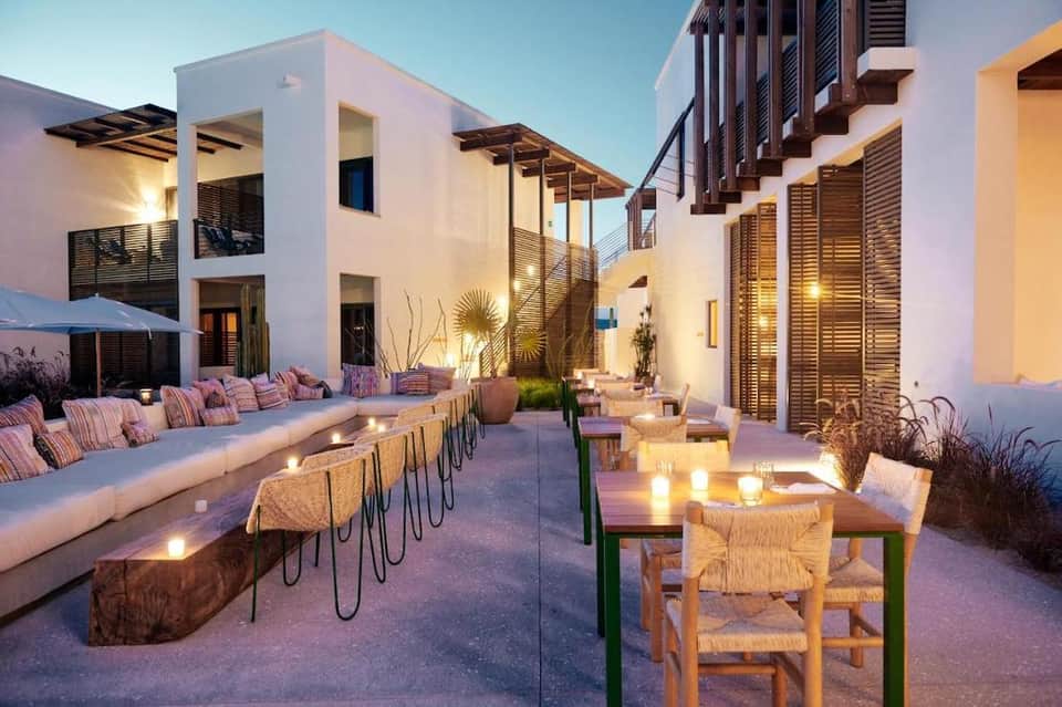 Contemporary resort courtyard at dusk with white buildings, pink striped cushions, lounge seating, and warm lighting