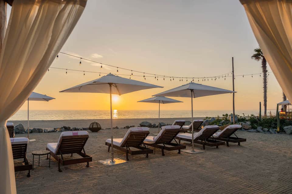 Beach sunset with lounge chairs, umbrellas, string lights, and ocean view at golden hour