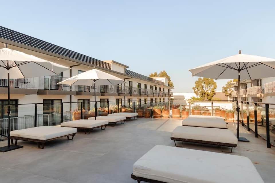 Modern rooftop terrace with lounge beds, white umbrellas, and desert landscape views