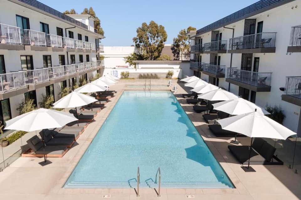 Luxury hotel courtyard with rectangular pool, white umbrellas, black loungers, and surrounding apartments