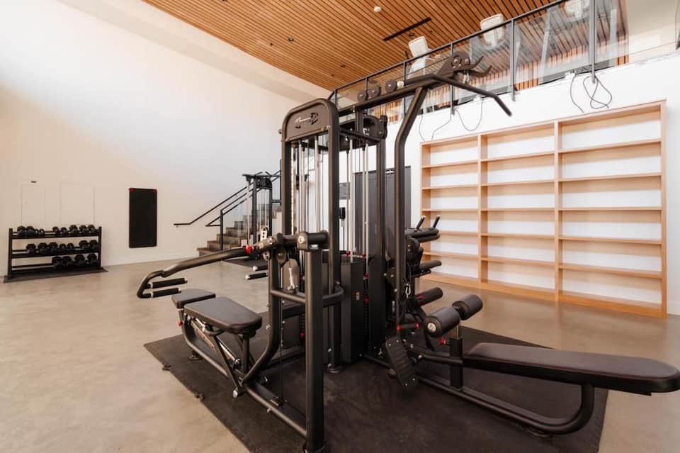 Modern fitness center with multi-station exercise equipment, dumbbells, and wooden accent wall