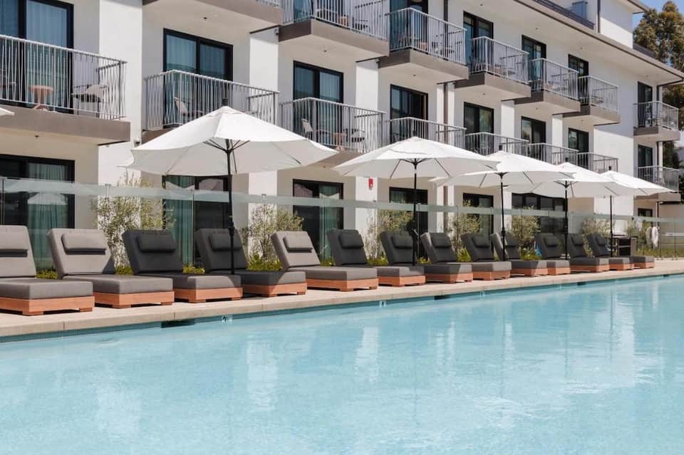 Resort pool with lounge chairs, white umbrellas, and multi-story white building with balconies