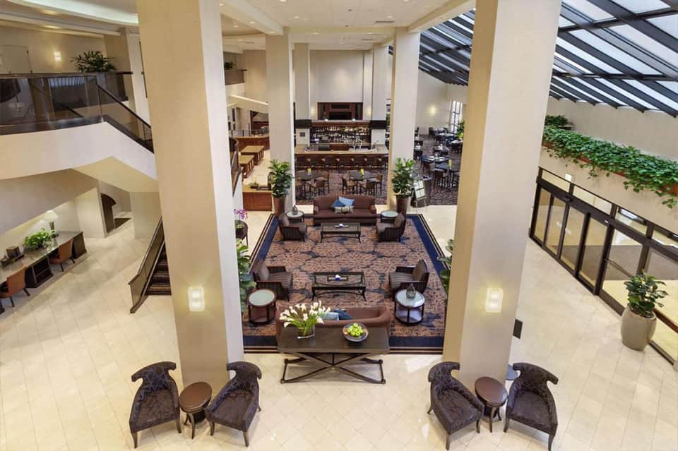 Multi-level hotel lobby atrium with seating areas, bar, decorative columns, and geometric railings.
