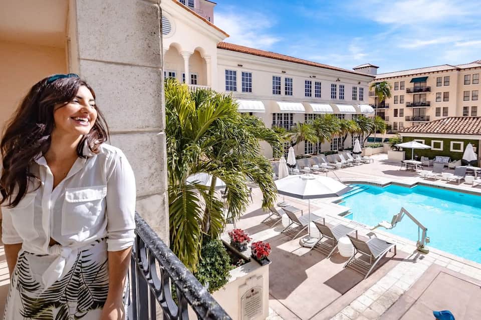 Woman on balcony overlooking resort courtyard with pool and palm trees