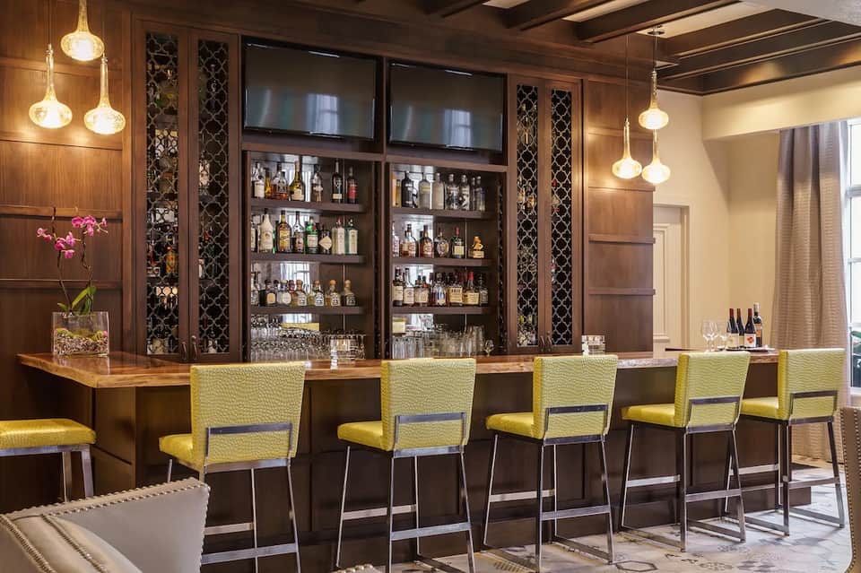 Upscale hotel bar with wooden cabinetry, yellow bar stools, and illuminated pendant lights