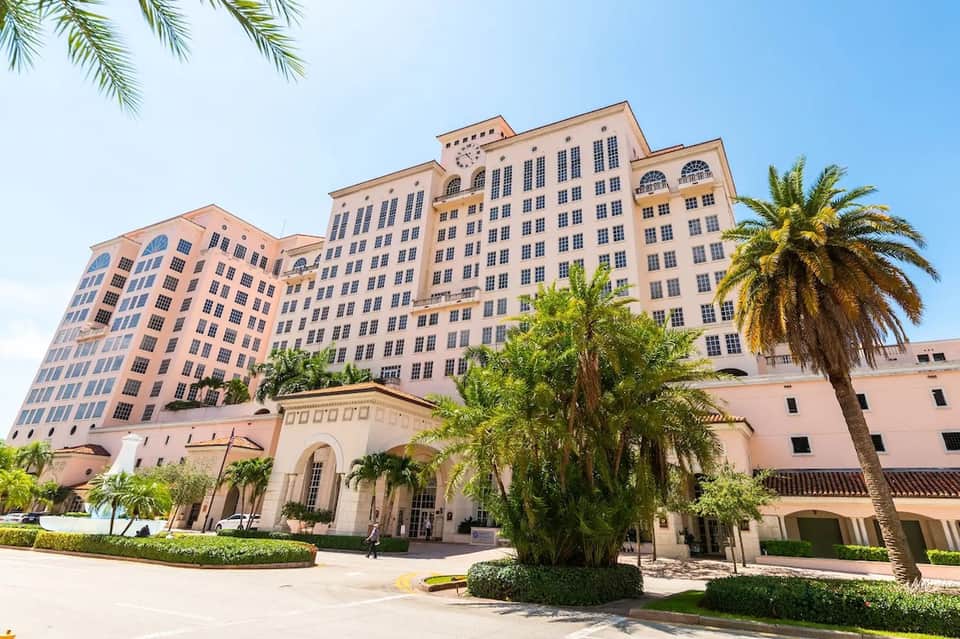 Elegant pink historic hotel building with classical architecture surrounded by palm trees and manicured grounds